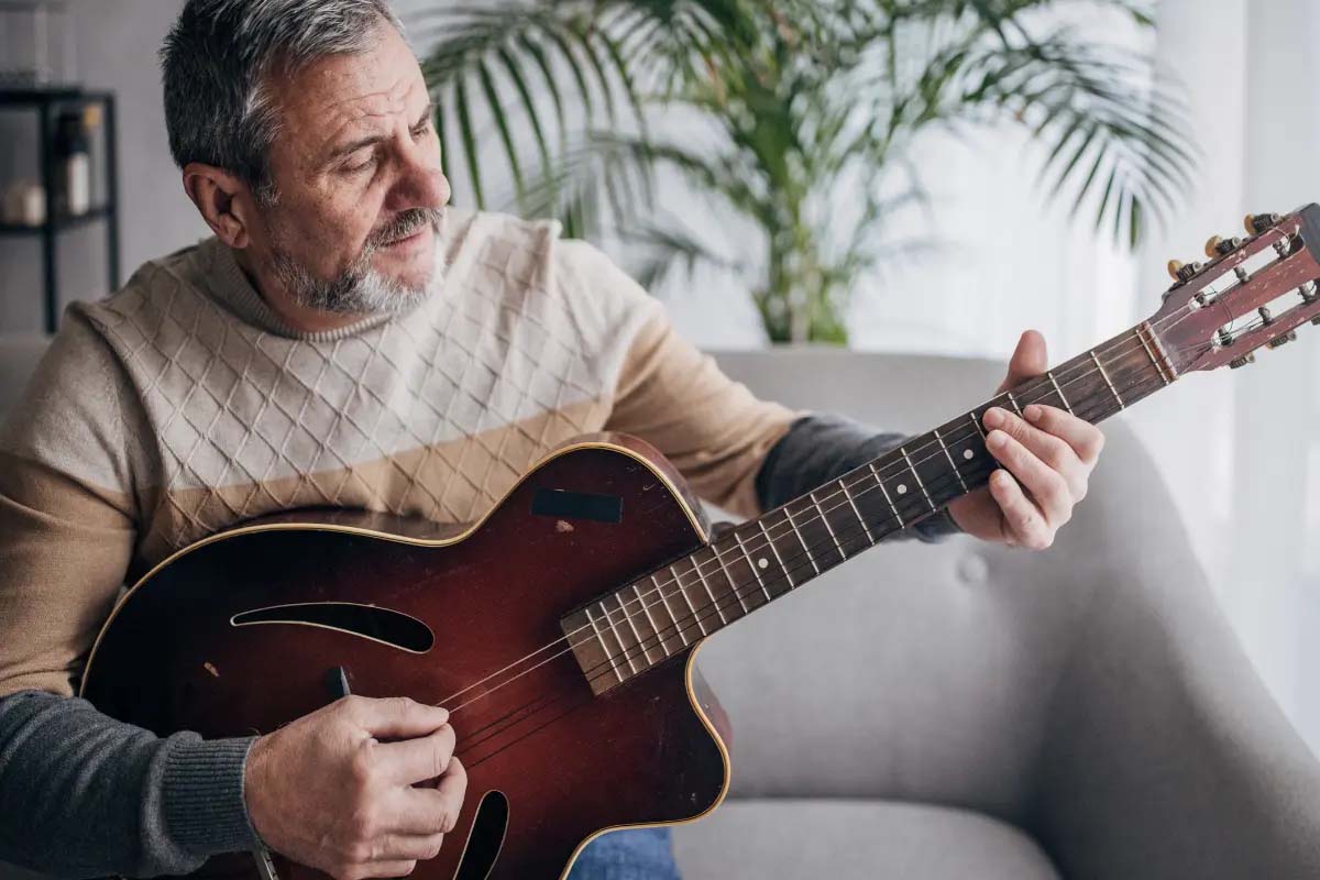 Senior man playing a guitar indoors, relaxed ambiance.